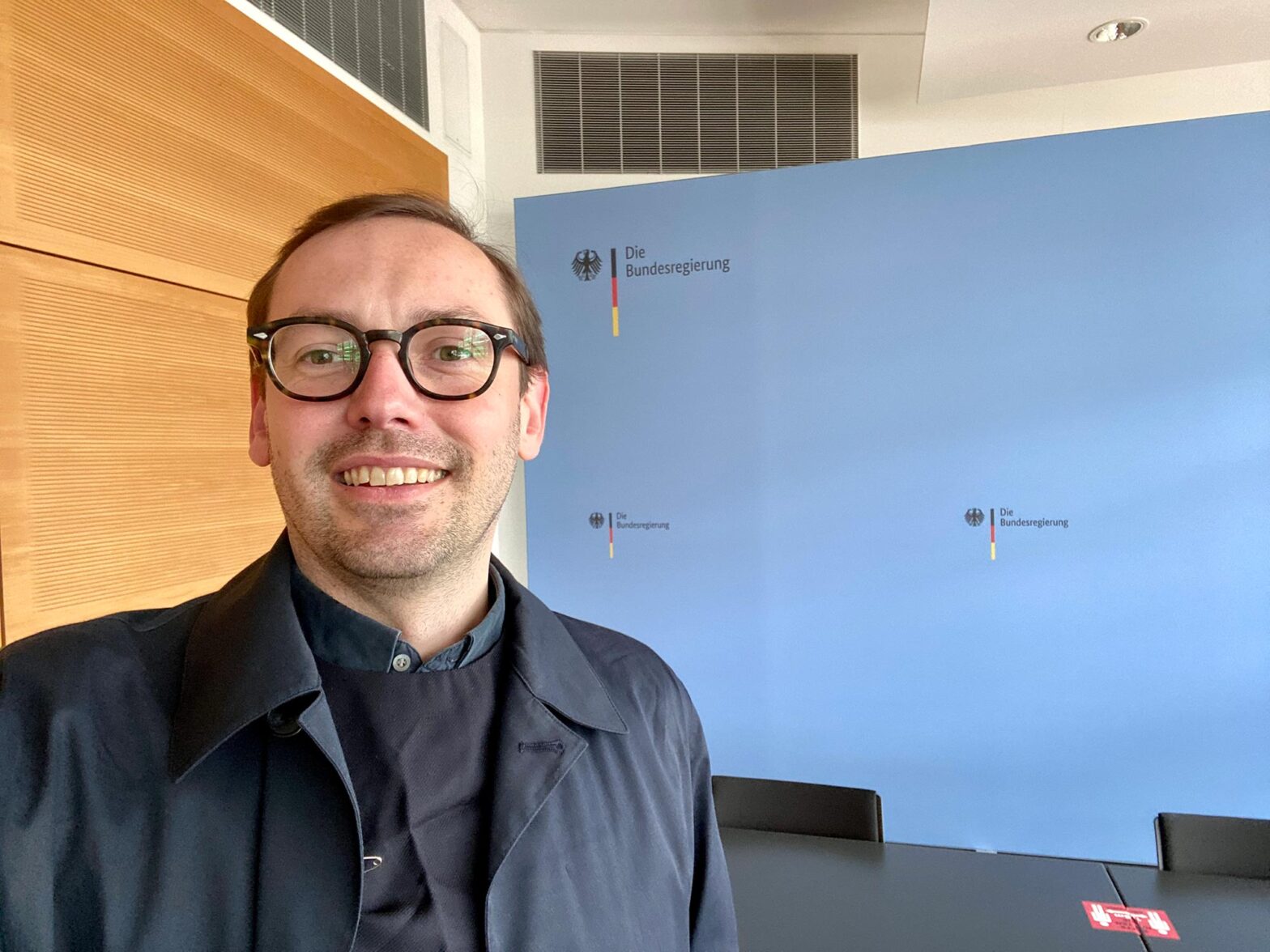 Selfie of Martin Jordan, Head of Design at the German government’s Digital Service in a press room of the Federal Press and Information Office that’s usually used for important press conferences and has the Federal Government’s logo in the back