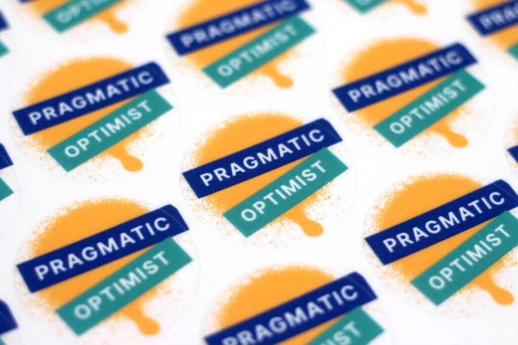 A sheet of stickers saying pragmatic optimist with an artificial spray can splatter behind