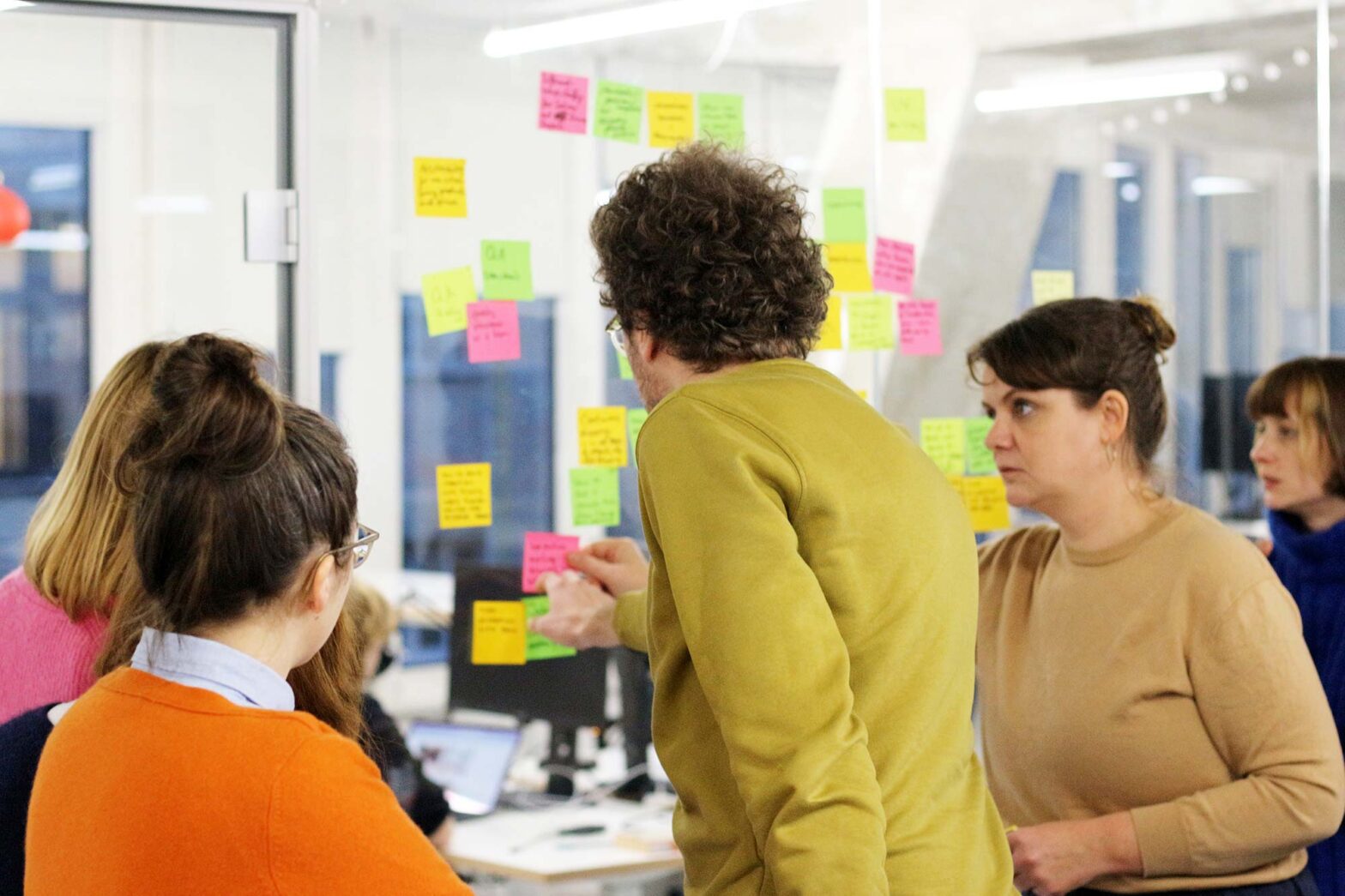 6 members of the DigitalService design team collecting colourful sticky notes on a glass wall in a modern office space