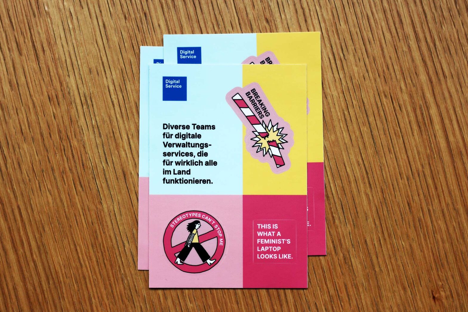 A little pile of sticker sheets with 3 colourful stickers: 1 says “breaking barriers” and shows a barrier being broken, another sticker says “stereotypes can’t stop me” and shows a hand-drawn person with longer hair passing a ‘no entry’ sign, and a third sticker saying “this is what a feminist’s laptop looks like” in all capital letters.
