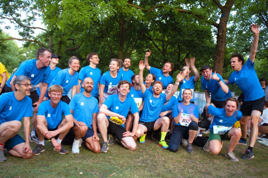 Group photo of 20 DigitalService employees in blue running shirts and short in a park