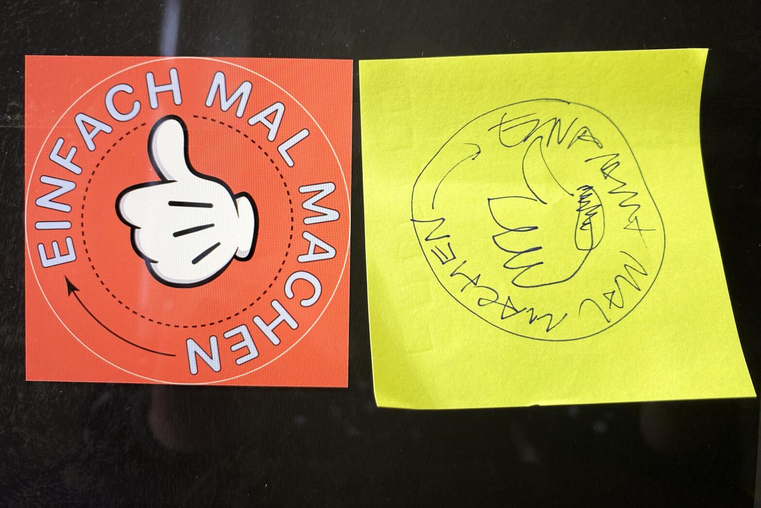 Two design versions of the same design next to each other: A Mickey Mouse-style hand showing thumbs up inside a circle – the letter around saying: Just do it in German