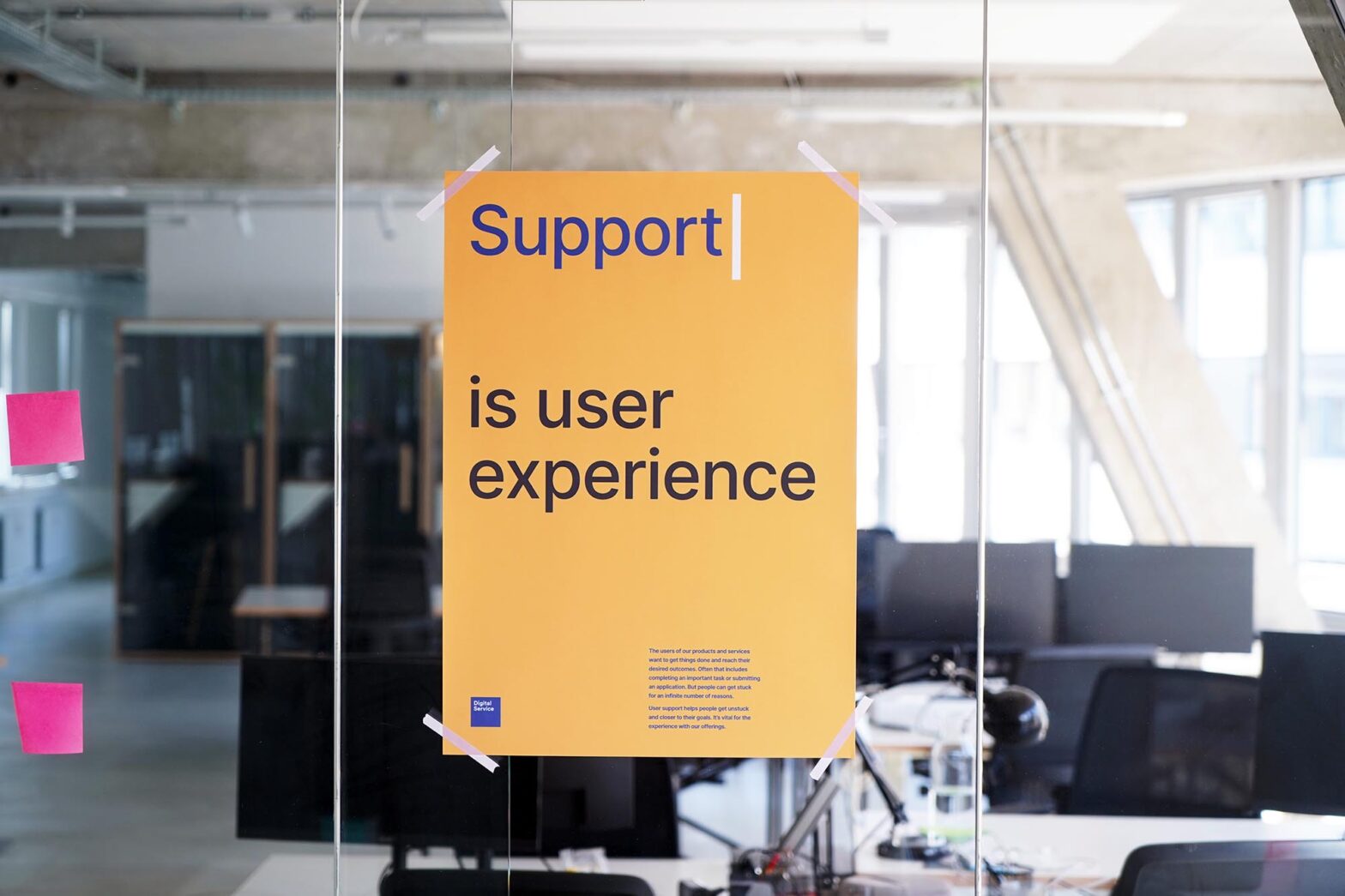 A yellow poster hanging on a glass wall in a modern looking office space, saying: Support is user experience