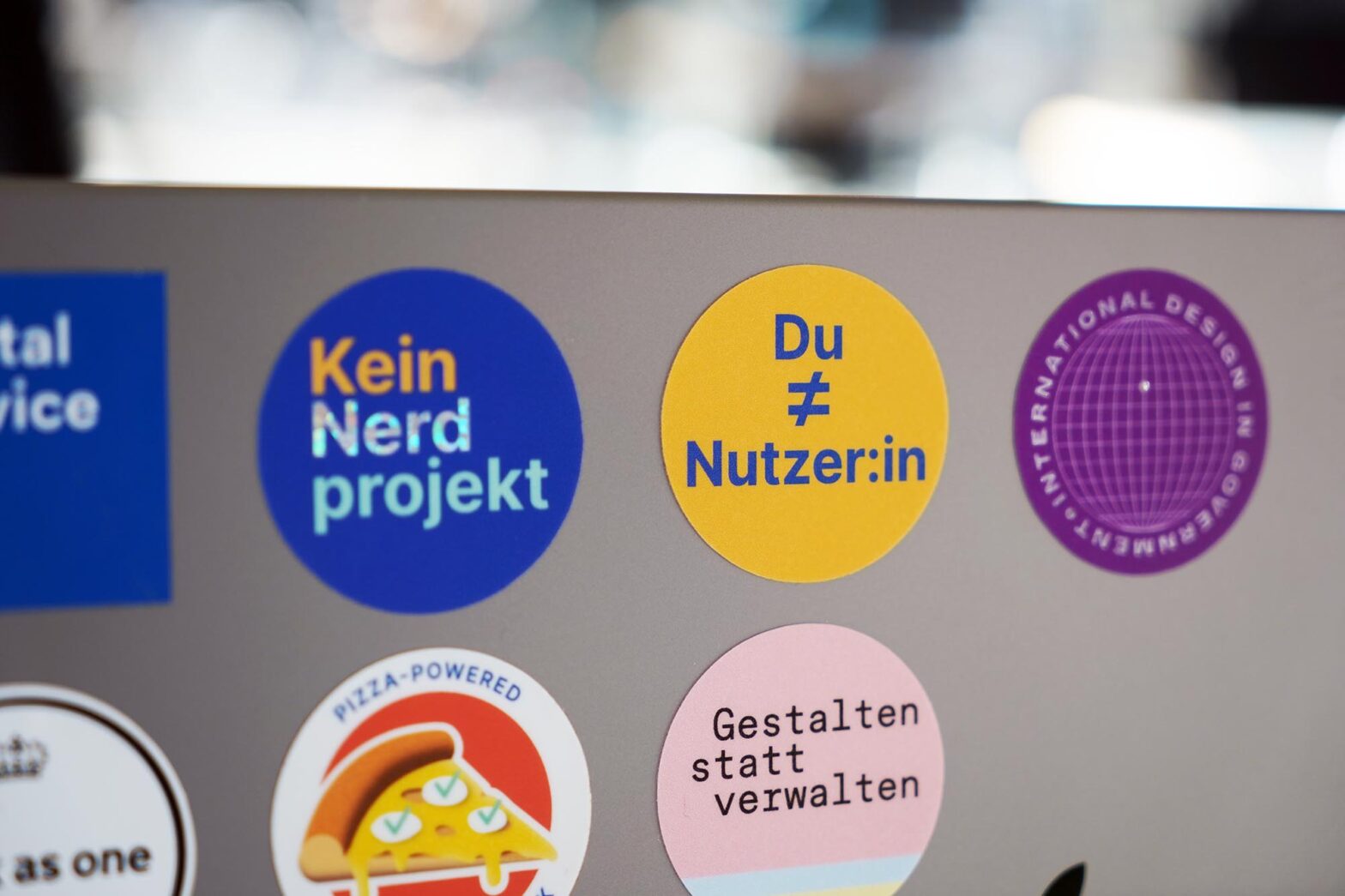 Mehrere bunte Sticker auf einem silbernen Laptop-Computer; ein gelber Sticker im Fokus sagt ›Du ungleich Nutzer:in‹