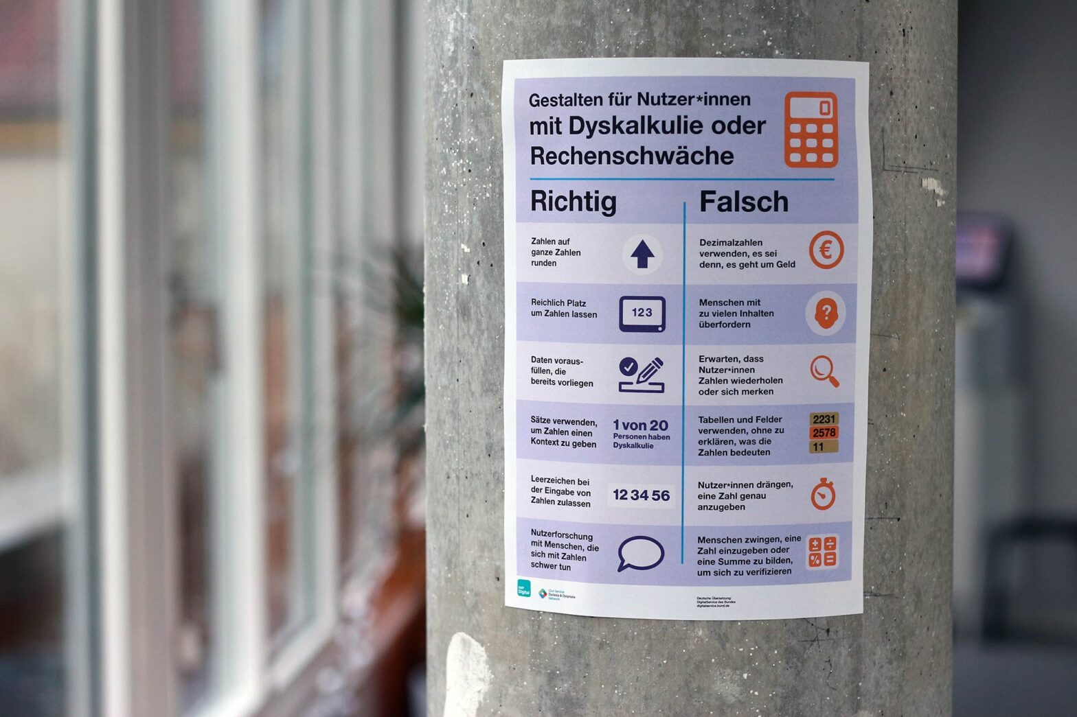 A small poster on a concrete wall saying in German: “Designing for people with dyscalculia and low numeracy” with a list of 6 DOs and 6 DO NOTs and little illustrations for all 12 of these tips