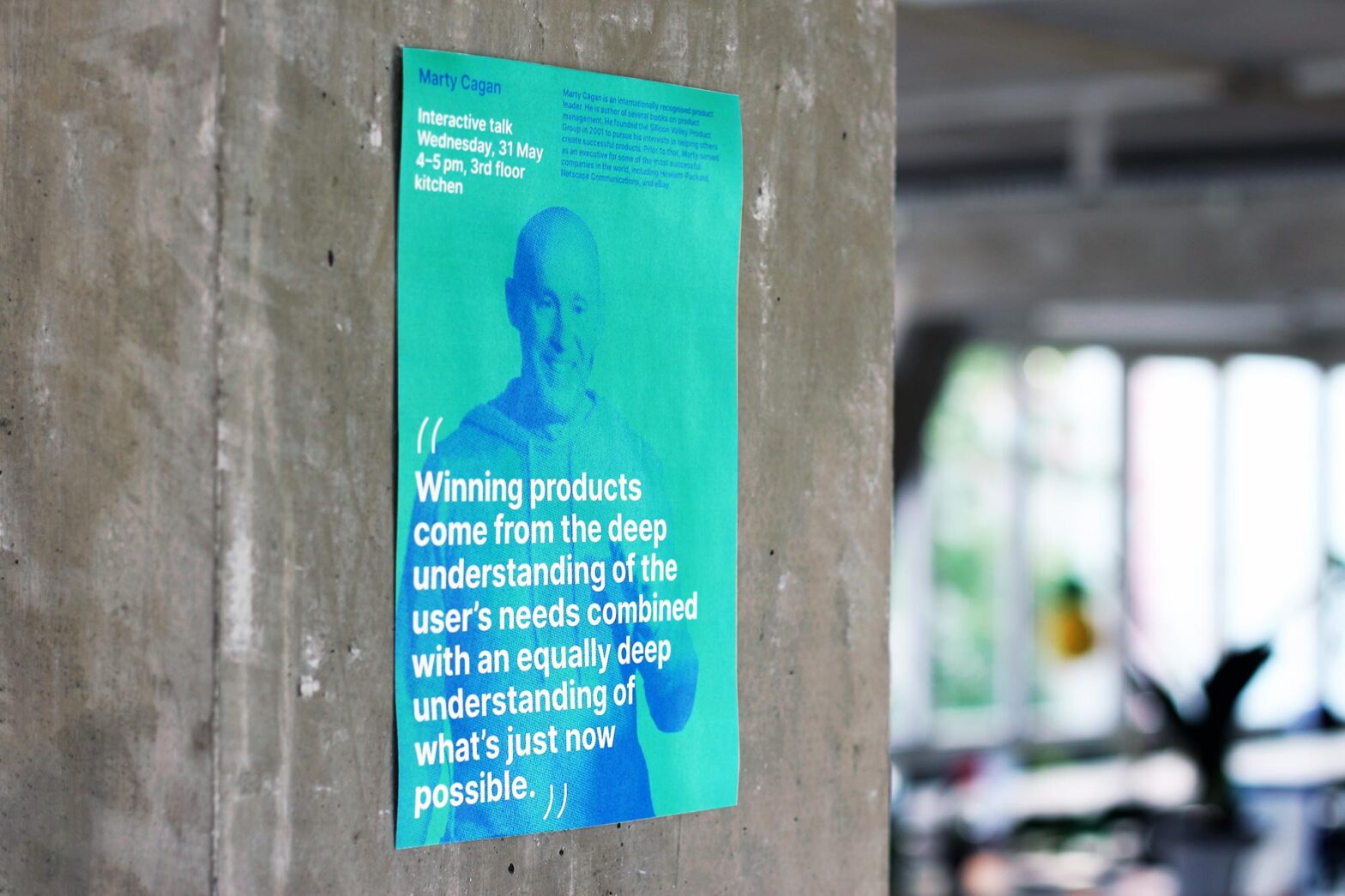 A bright green poster on a bare concrete wall in an office space, it shows the picture of a middle-aged white man with a big quote: “Winning products come from the deep understanding of the user’s needs combined with an equally deep understanding of what’s just now possible.”
