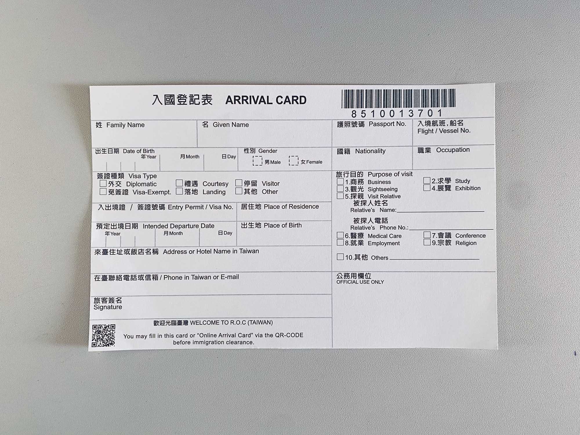 A small bilingual government form in a light grey surface – in traditional Chinese and English it says ‘ARRIVAL CARD’; it contains about two dozen fields including name, date of birth, address, passport number, purpose of visit