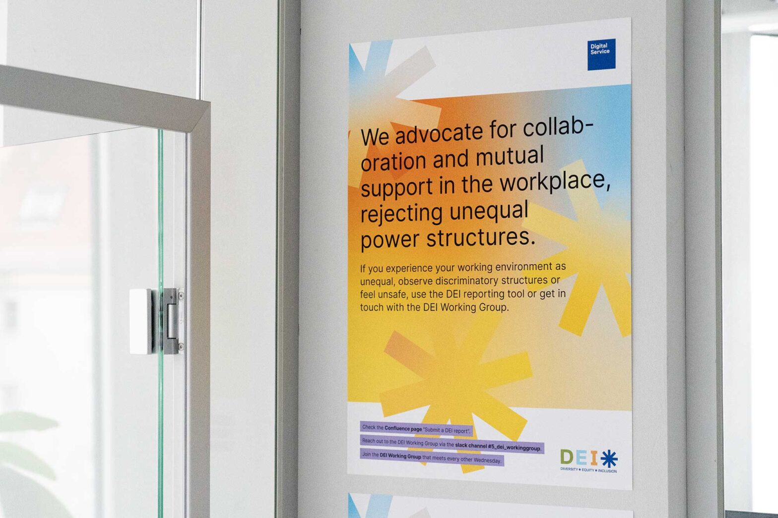 A colourful poster with the logo of DEI – diversity, equity, inclusion – in the corner of a well-lit office wall with a big sentence: “We advocate for collaboration and mutal support in the workplace, rejecting unequal power structures”