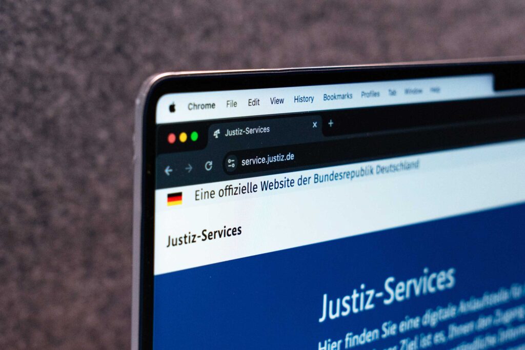 Activate to view larger image,
"Close-up of a laptop screen displaying the Justiz-Services website, an official website of the Federal Republic of Germany, featuring a German flag in the header, a black URL bar showing 'service.justiz.de,' and a blue section with white text introducing digital judicial services."