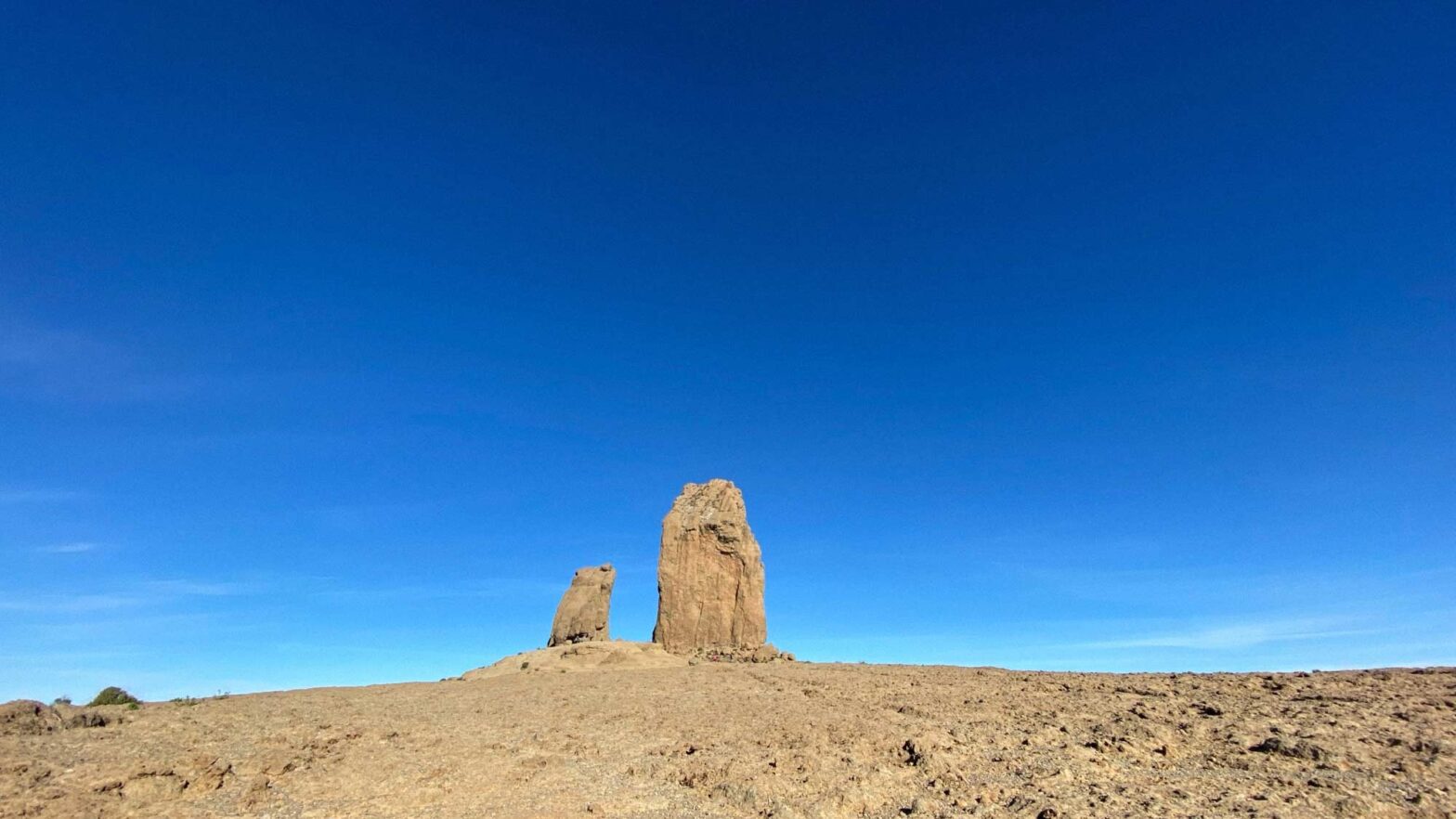 Two larger rock formations in a stone desert: one rock being about two times the size of the other; sky is clear blue with no clouds