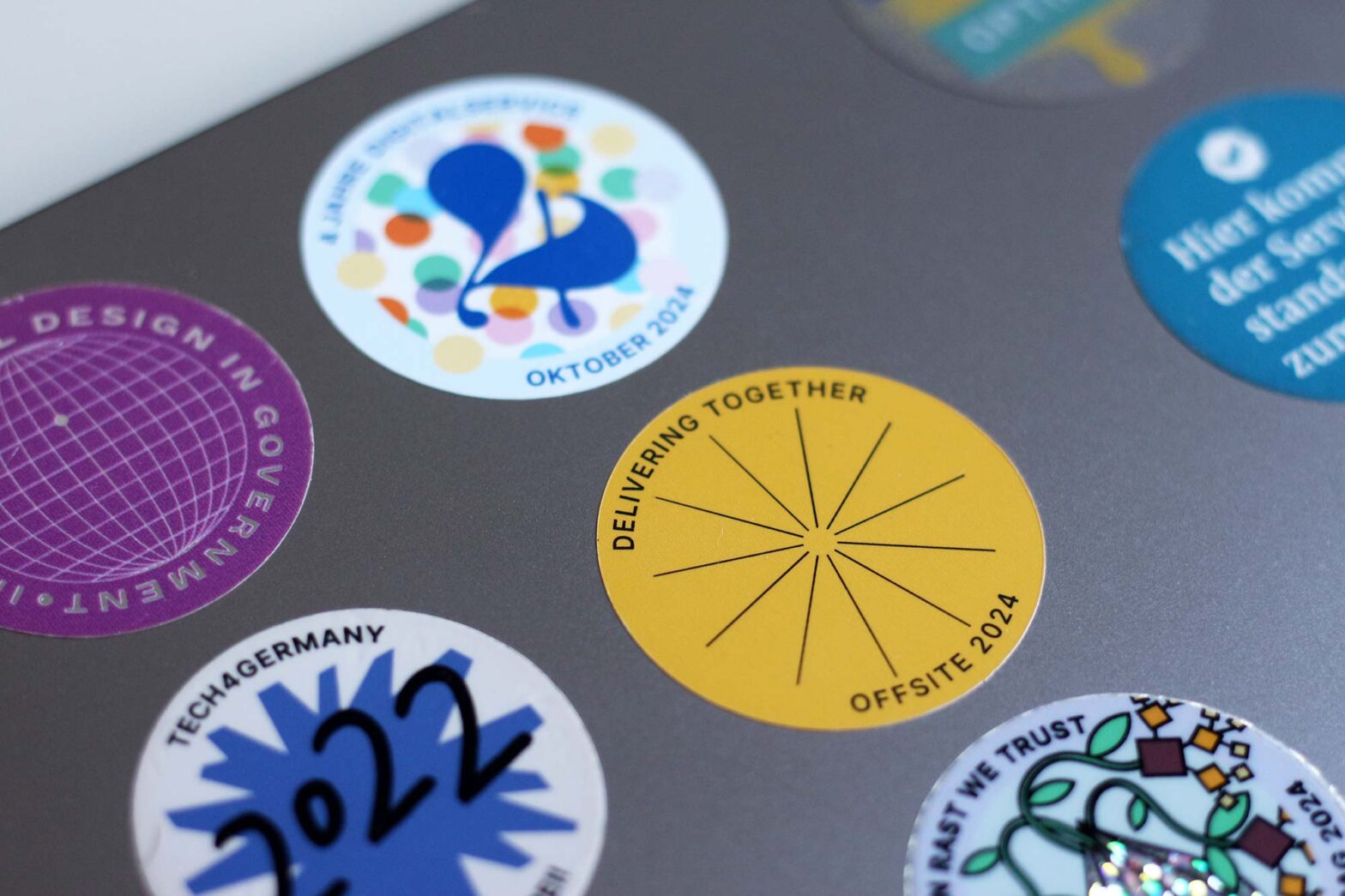 Stickers of different colours and designs on a laptop computer, the sticker in focus says “Delivering together, Offsite 2024”