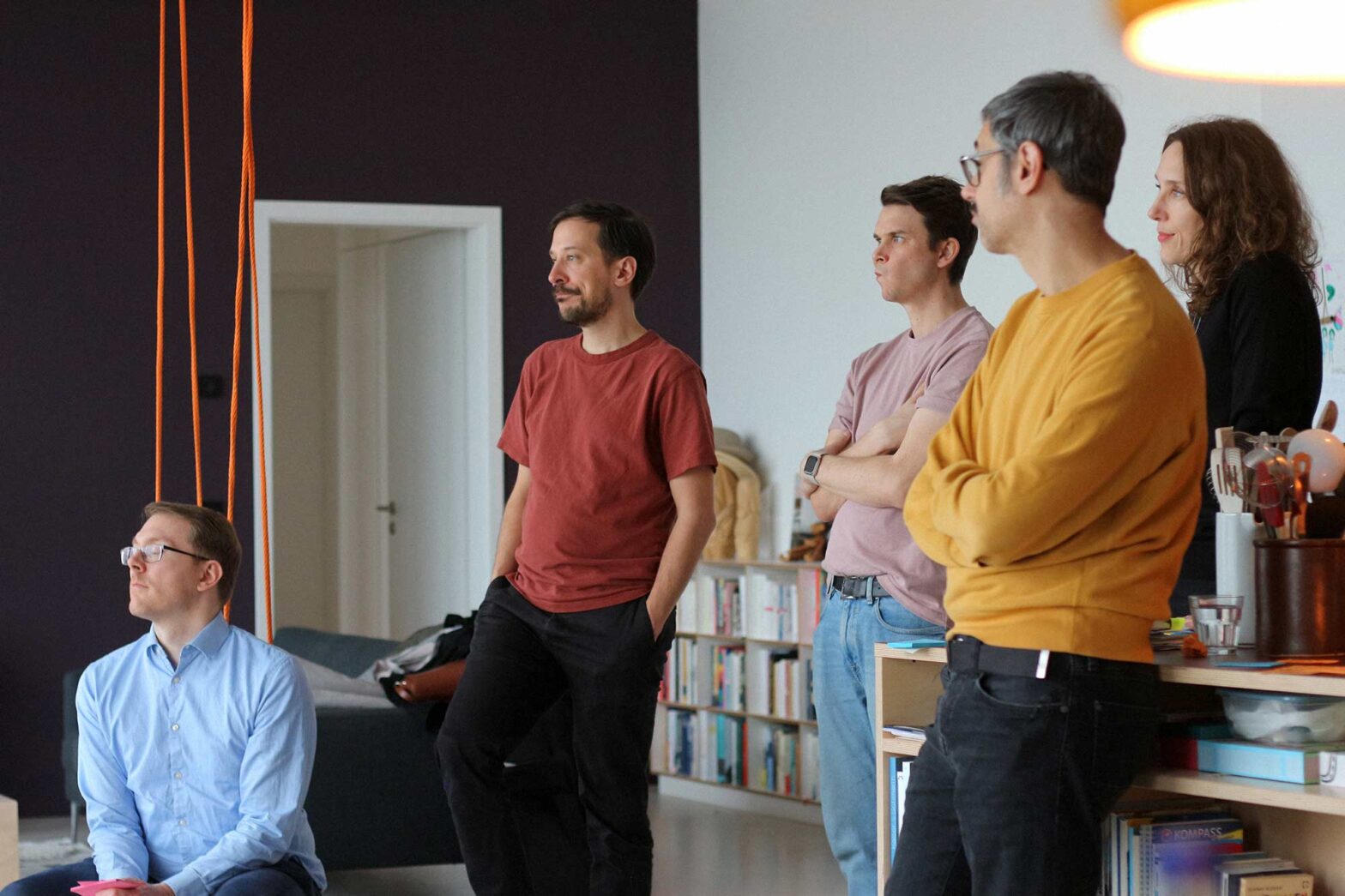 5 middle-aged people, 4 men and 1 woman, with light skin and informal clothes in a modern space all looking into the same direction, a swing is hanging from the ceiling