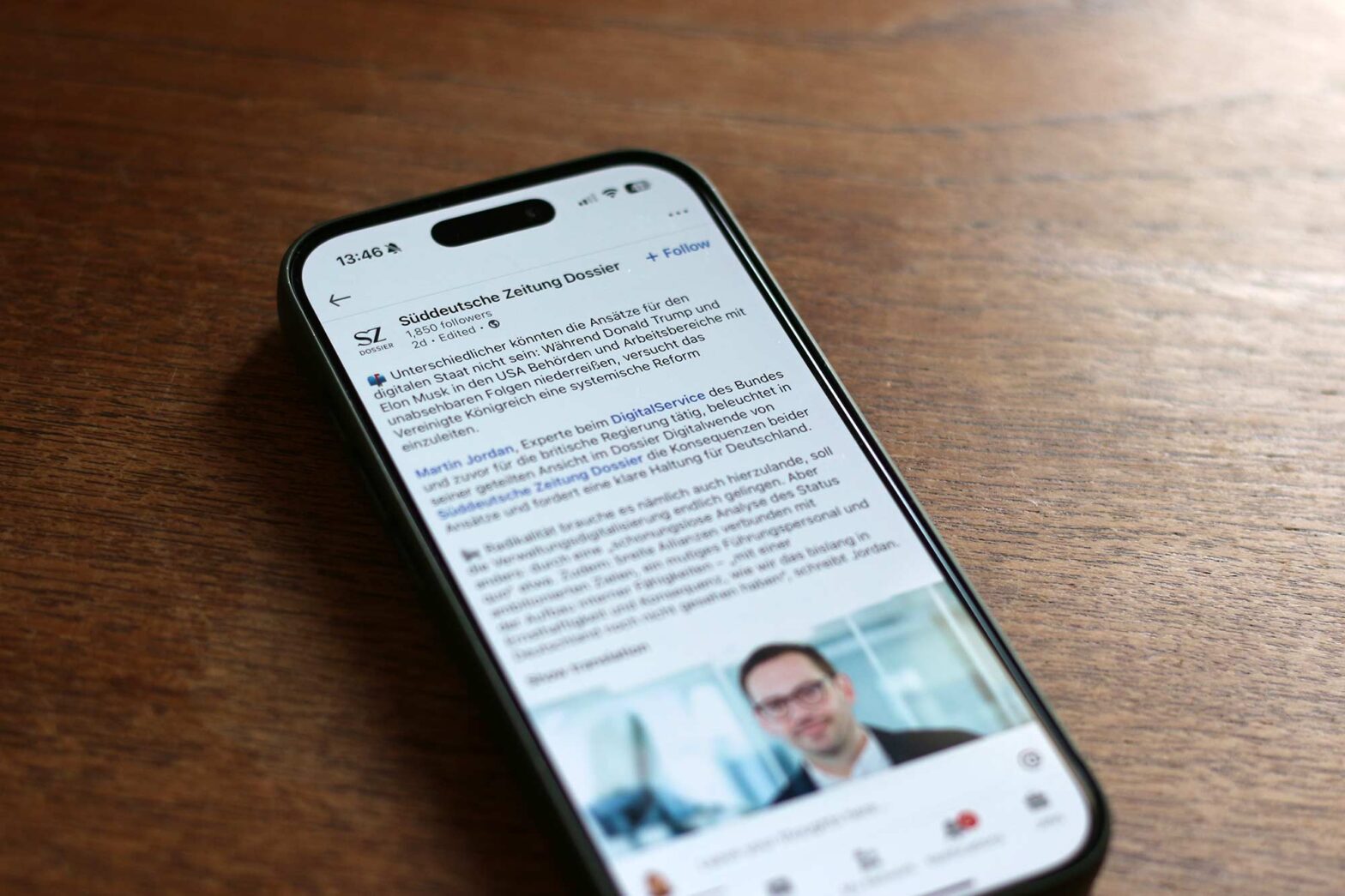 A phone on a wooden table displaying a post of Sueddeutsche Zeitung Dossier featuring an article from Martin Jordan with 3 short paragraphs of text and a picture of him