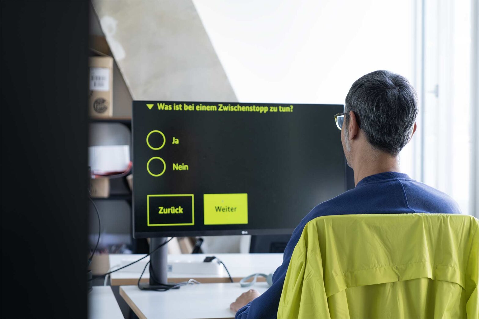 A man with grey hair is sitting in a chair in front of a big computer monitor, displaying a much magnified form in bright yellow and black colours.