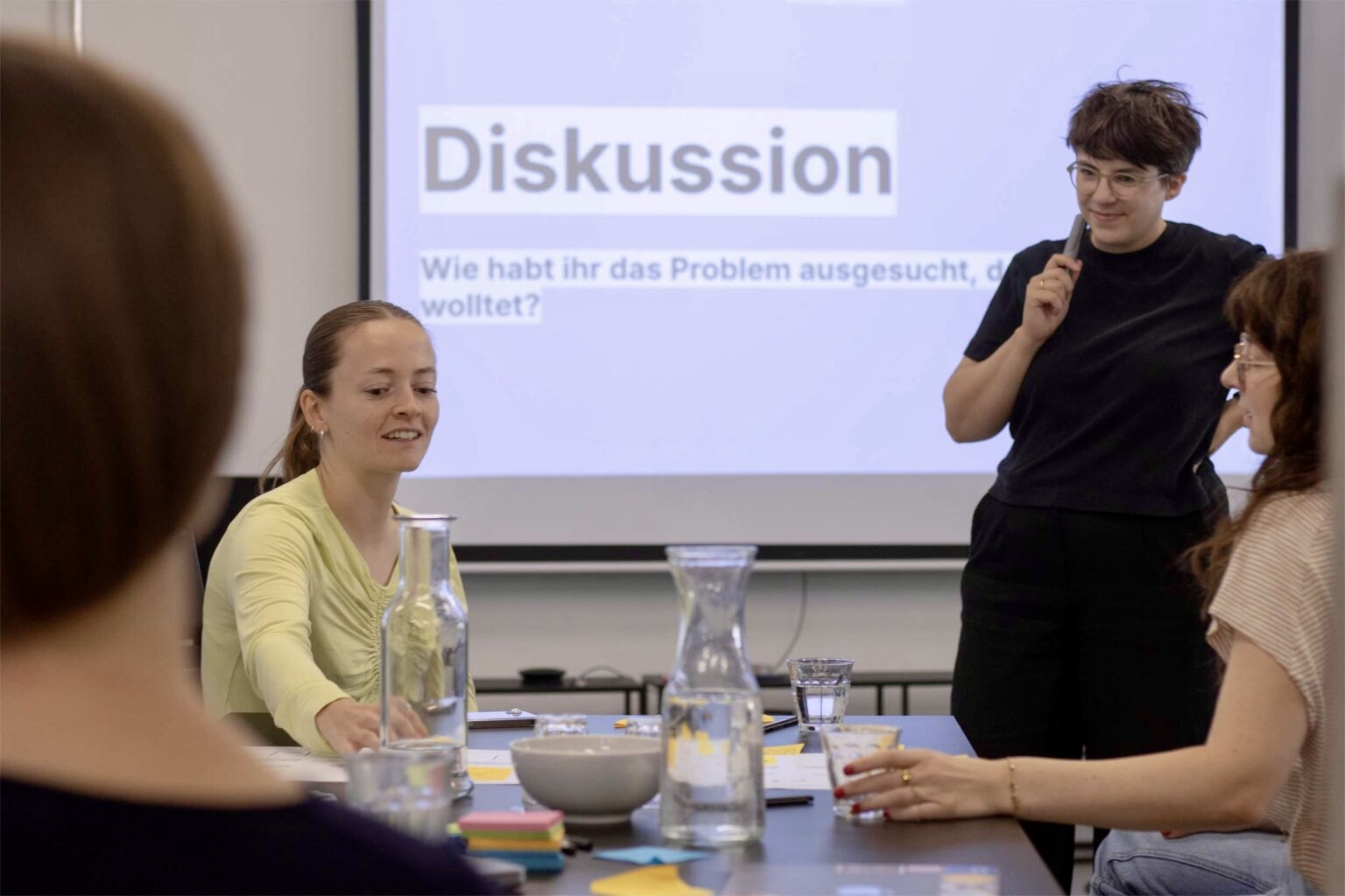 4 women with light skin in a workshop setting with a projected screen behind them saying “Discussion”