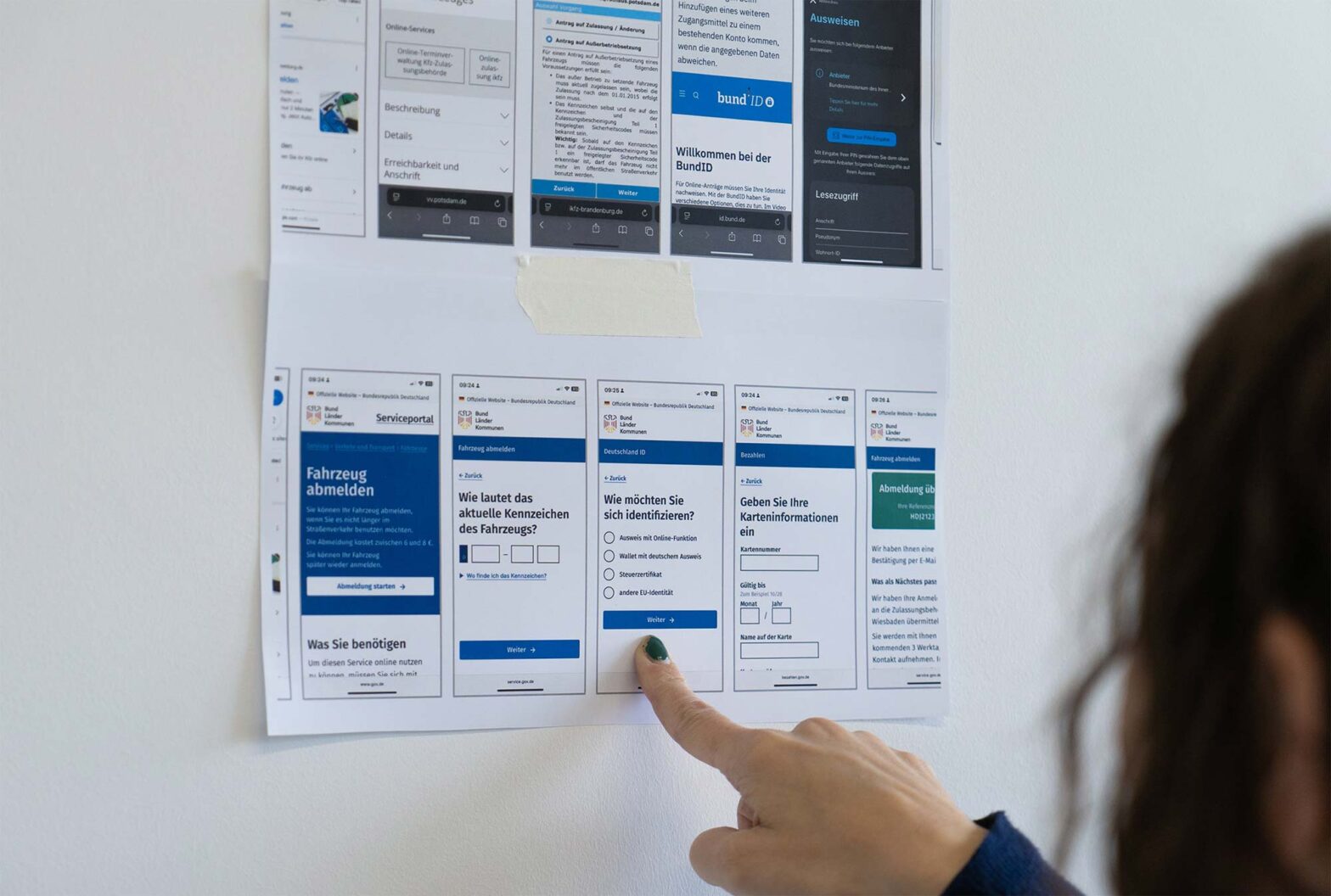 A person pointing at one of two printouts, these show 2 rows of screens: the upper one of vastly different visual designs, the lower one with a neatly consistent visual appearance for the ‘taking a car off the road’ service