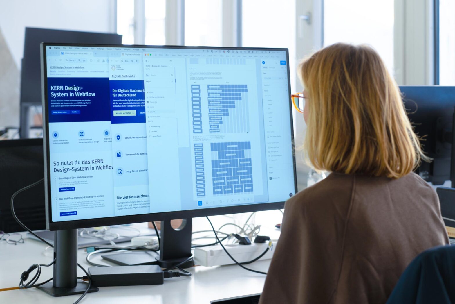 A person sits in front of a large computer screen displaying various windows: with the KERN design system, the digital umbrella brand and a visual grid system.