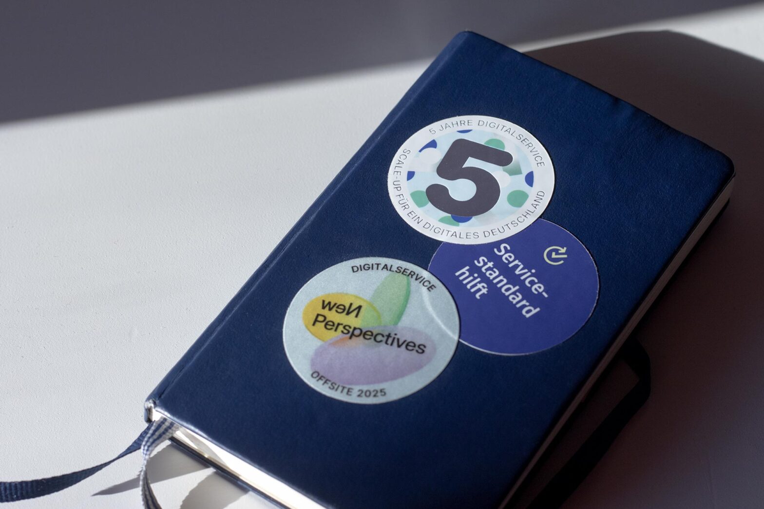 Dark blue notebook with 3 stickers" one with a big 5 that says 5 years DigitalService