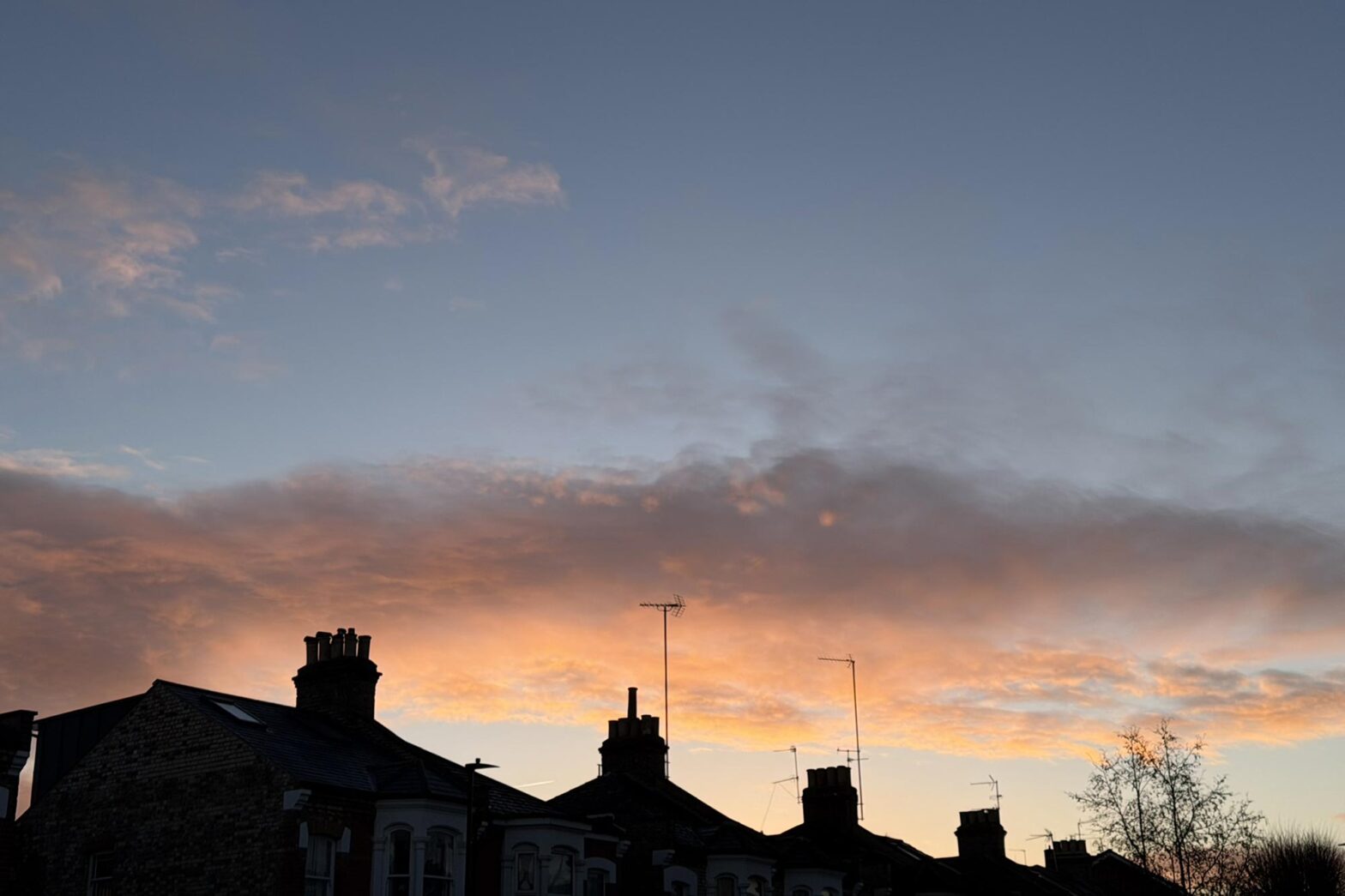 A beautiful sunset with a salmon-coloured cloud behind a row of houses with prominent chimneys