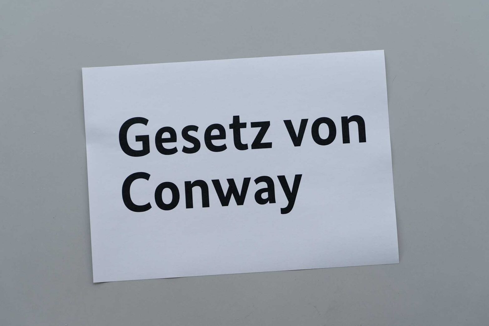 A white sheet of paper on a grey background, reading in German: “Conway’s law”